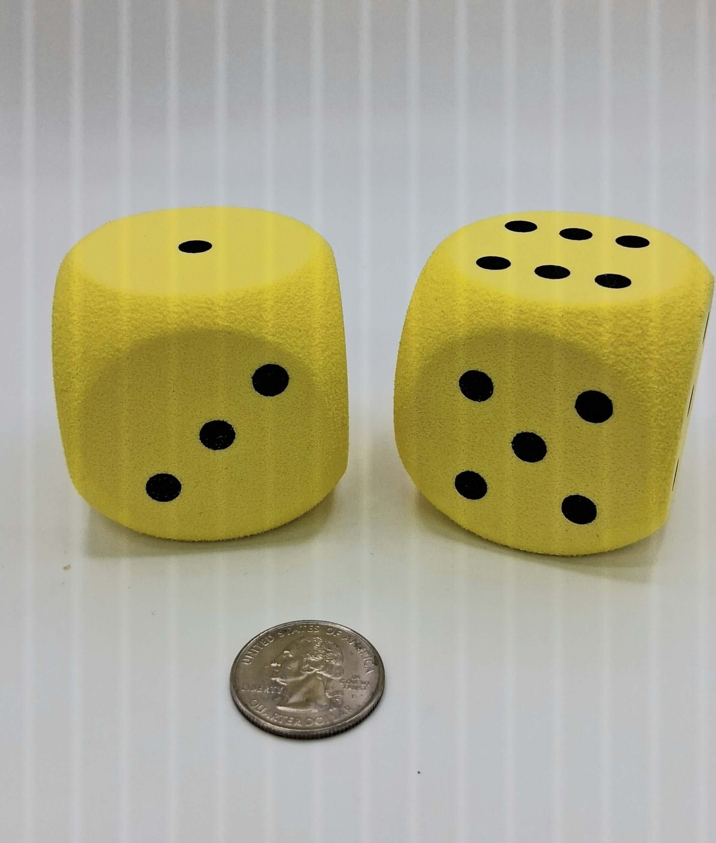 Oversized soft foam yellow dice displayed next to a quarter for size comparison with bold black dots.