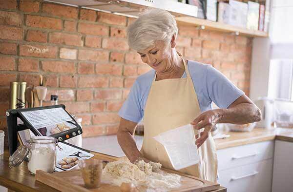 Elderly woman using CloverBook LITE video magnifier in kitchen while baking.