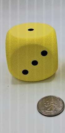 Oversized soft foam yellow dice next to a quarter for scale, showing its soft texture and bold black dots.