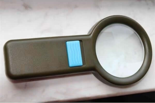 3x 10 LED Illuminated Pocket Magnifier with blue button on a marble surface, ideal for detailed inspection and reading.
