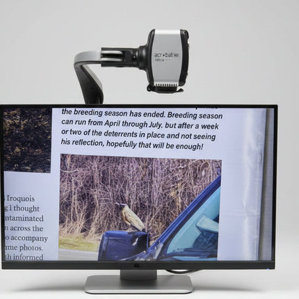 Monitor displaying text and images on a desk with a remote control and paper.