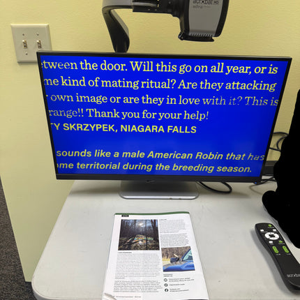 Digital display with blue screen text on a wall-mounted device, next to a newspaper.