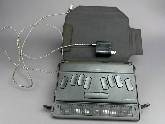used BrailleNote Touch 32 Plus Braille note taker tablet with 32-cell Braille display, charger, and protective case on gray background