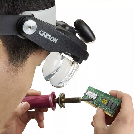 Person using an LED lighted head magnifier to solder a circuit board with a precision tool.
