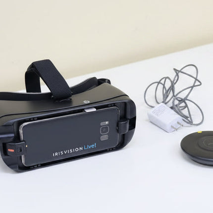 Black VR headset with 'IrisVisionLive!' branding on a wooden surface, accompanied by a power adapter and cable.