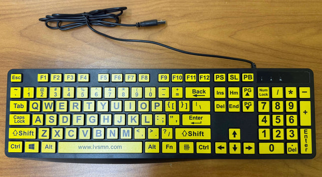 A black computer keyboard with bright yellow function keys and a black cable, placed on a wooden desk.