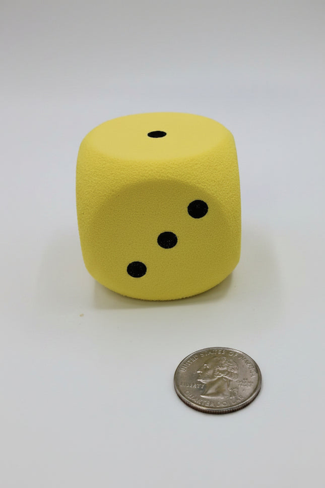 Oversized soft foam yellow dice next to a quarter for scale, showing its soft texture and bold black dots.