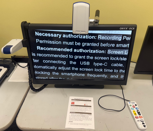 Small screen displaying text on a desk with a remote control and paper in the foreground.