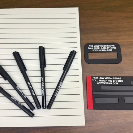 low vision writing aids kit with bold line paper, bold pens, signature guide and check writing guide on wooden desk