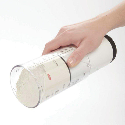 Hand holding an adjustable measuring cup for low vision filled with flour, showcasing the easy measurement features.