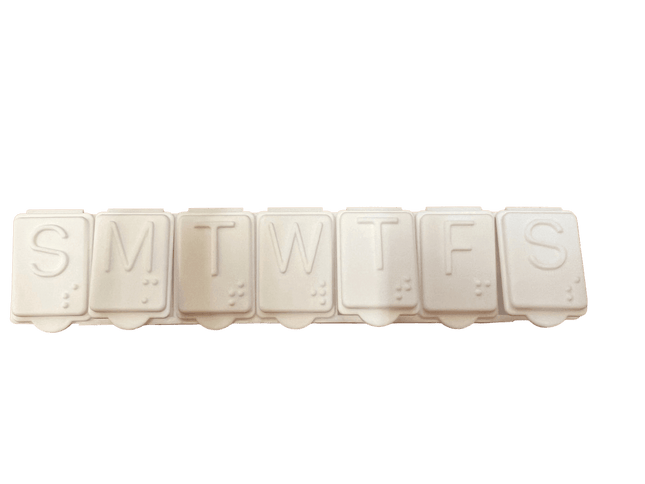 Brailled weekly pill organizer with compartments for each day of the week, featuring standard letters and Braille markings.