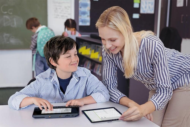 A teacher assists a student using a Braille note taker tablet in a classroom setting.
