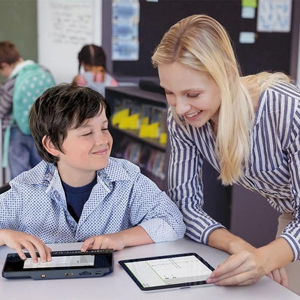 A teacher assists a child using a Braille notetaker with 32-cell display in a classroom setting.