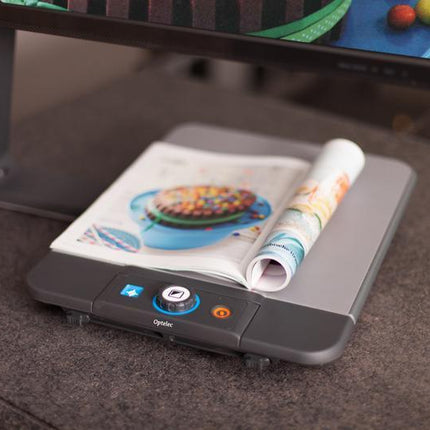 Desktop video magnifier for low vision with a magazine on a reading platform.