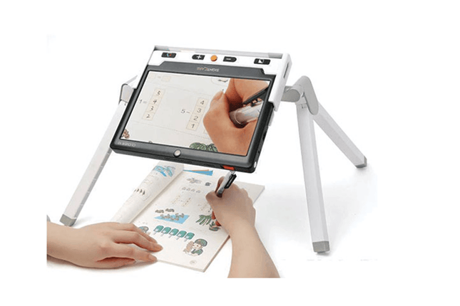 Clover 10 HD video magnifier with optional stand, showing a user writing on paper with the device.