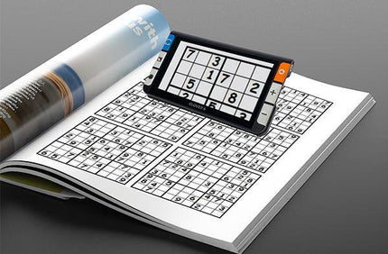 Clover 6 HD handheld video magnifier being used to read Sudoku puzzles in a magazine.