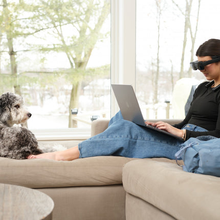 Woman using eSight Go low-vision headset while sitting on a couch with a dog, enhancing vision and mobility.