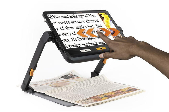 Portable video magnifier for low vision in use with a hand adjusting the display while reading a magazine.