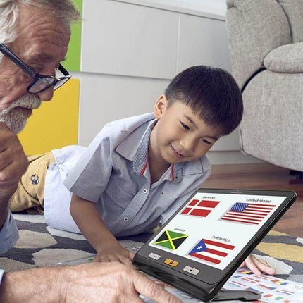 A senior man and a child using a portable video magnifier for low vision to read country flags on a colorful rug.