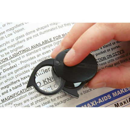 Folding Pocket Magnifier shown in use with a hand holding it over printed text for enhanced readability.