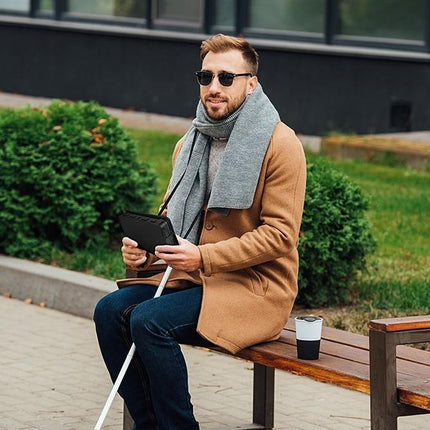 Man using Humanware Brailliant BI 20X braille display while sitting on a bench outdoors.