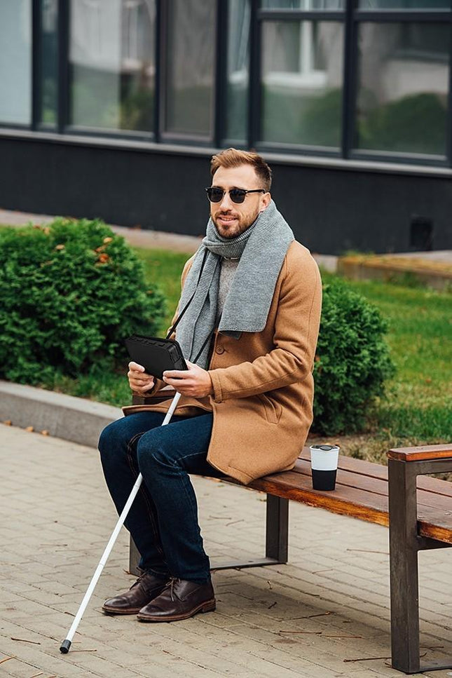 Man using Humanware Brailliant BI 20X braille display while sitting on a bench outdoors.