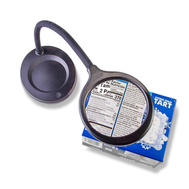 LED magnifier desk lamp illuminated over a food label on a box, showcasing its flexible neck and 5X power spot lens.