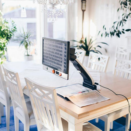 MagniLink One video magnifier for low vision on a dining table, showcasing clear text display and user-friendly design.