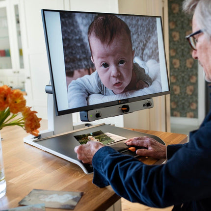 An elderly man using a 24 inch video magnifier for low vision to view photos of a baby on the screen.
