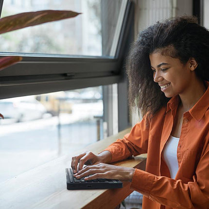 Woman using Mantis Q40 Braille Display at a sunlit window, smiling while engaged with the device.