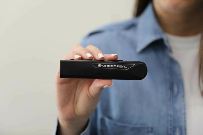 User holding the OrCam Read text to speech device for reading printed text easily.