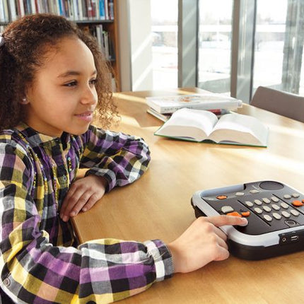 Girl using Victor Reader Stratus12 M on a table with books in a bright library setting.