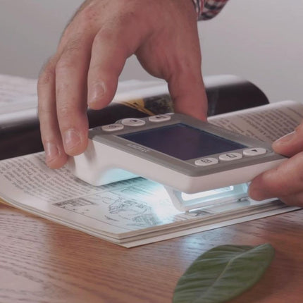 Person using Supersight handheld video magnifier on a book page to enhance readability.