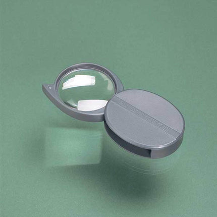 5X magnifying glass with swing case open on a green surface, showcasing its lens and protective cover.