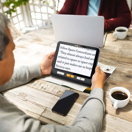 Person using Explore 8 handheld electronic magnifier to read text at a café, showcasing its large display.