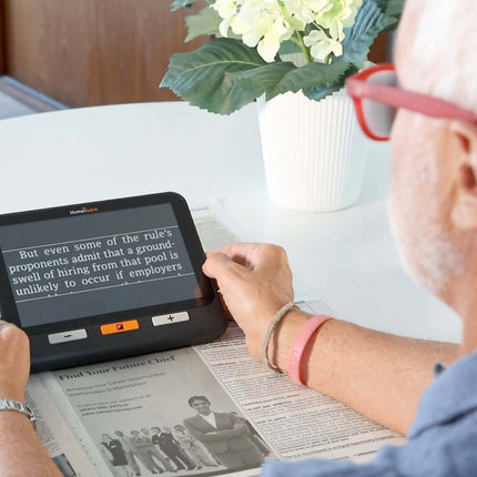 A user reading a newspaper with the Explore 8 handheld electronic magnifier on a table.