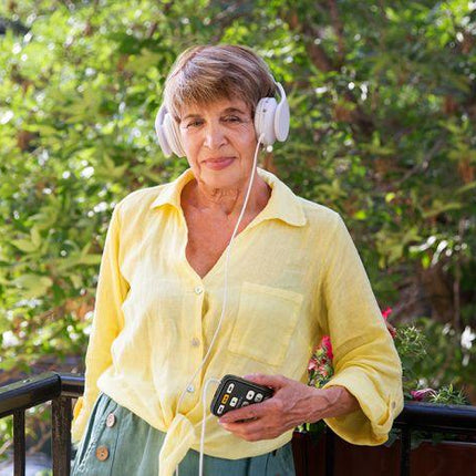 Woman in a yellow shirt using a handheld digital audio player for blind, enjoying music outdoors.