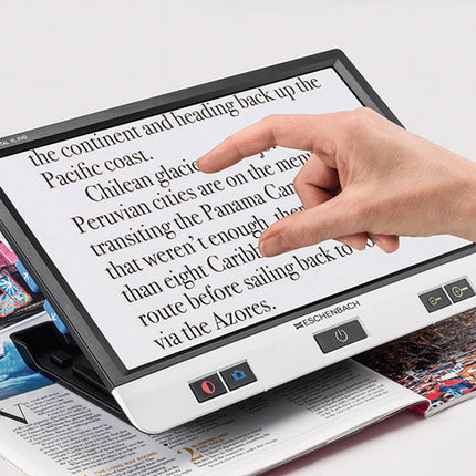 Person using a 12 inch touchscreen video magnifier to read text on a magazine.