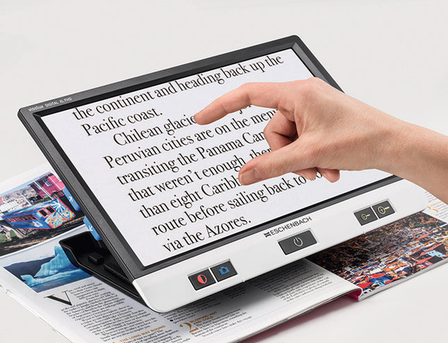 Person using a 12 inch touchscreen video magnifier to read text on a magazine.